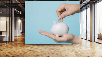 Hand saving a coin into piggy bank  on blue background for investment, business, finance and saving money concept. Wall mural