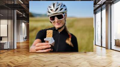 Female cyclist wearing cycling kit holding energy snack for endurance during bicycle training.Sport nutrition.Sport snack for cyclist.Granola energy bar. Wall mural