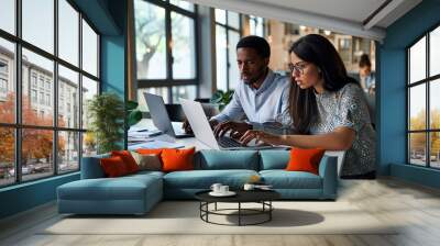 Diverse employees using laptop looking at business documents working in office. Busy professional team two African and Latin colleagues discussing marketing project plan sharing ideas, Generative AI Wall mural