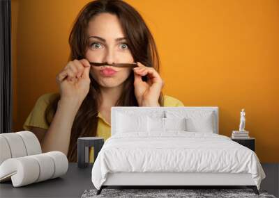 funny young woman who makes a mustache with a lock of her hair on an orange background Wall mural