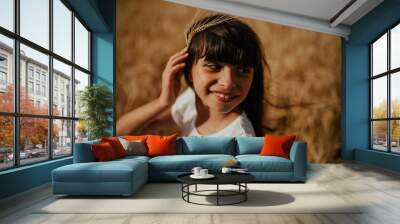 portrait of a girl having fun with an ear of wheat in a wheat field under a sunset Wall mural