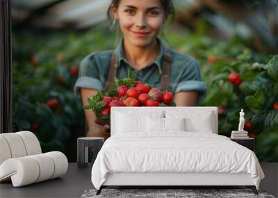 Smiling woman holding freshly picked strawberries in a lush, green garden setting, showcasing organic fruit harvest and gardening joy. Wall mural