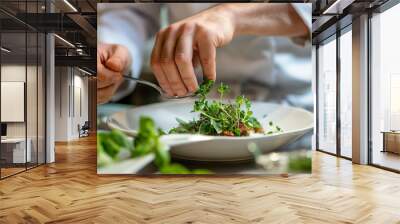 A professional chef carefully adds fresh herbs to a gourmet dish, enhancing its presentation in a bustling restaurant kitchen during dinner service Wall mural