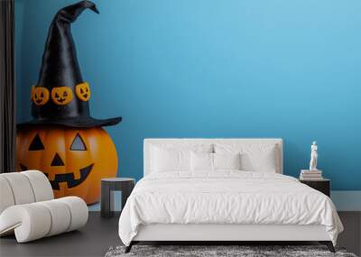 A vibrant orange pumpkin wearing a witch hat sits against a clear blue backdrop, creating a playful Halloween atmosphere that's ideal for autumn festivities, copy space Wall mural