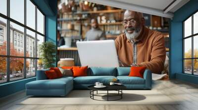 A middle aged African American man using a laptop in a coffee shop. Wall mural