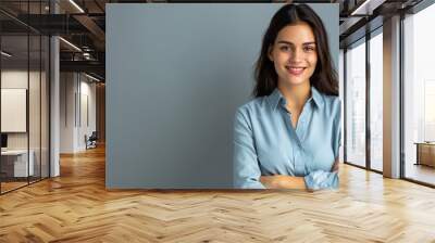 Happy young smiling confident professional business woman wearing blue shirt, pretty stylish female executive looking at camera, standing arms crossed isolated on gray background Wall mural