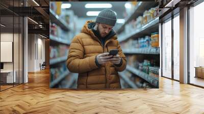 A man standing in a supermarket aisle, looking at his smartphone while shopping Wall mural