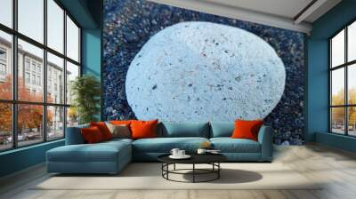 blue background. a round white stone among the black sand and pebbles. Close up Wall mural