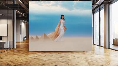  young beautiful woman model image Queen Cleopatra walks in desert Egyptian pyramids. Creative retro traditional gold jewelry bob hair cut. White satin long vintage dress, orange silk cape fly train Wall mural