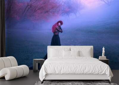 A sad lady in a black dress unhappy wanders in the fog. Background of autumn trees and hills. A lonely bird flies. A woman hugs her head in grief and cries. Pink hair. Art photo from the back, no face Wall mural