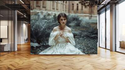 An incredibly beautiful princess sits in the castle garden amid the fern and moss. A beautiful, frightened face. Big sad eyes. Collected hair - a neat hair. On the lady - an old ivory dress. Art photo Wall mural