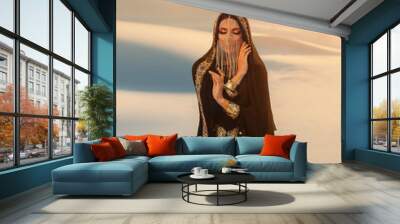 Beautiful mysterious arab woman Queen in black, muslim dress. head with silk handkerchief, golden chains hides face. A Fantasy Girl oriental princess walks in desert. art background yellow sand sunset Wall mural