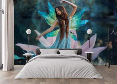 Beautiful young fantasy woman in the image of a river fairy dances on a water lily flower. A long silk dress flies in the wind, butterfly wings glisten. Background evening dark nature, blue lake. Wall mural