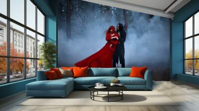 Blurred silhouette of a Gothic couple dancing in the fog. A vampire man in black tailcoat with long hair embraces seduces a woman in a long red medieval dress. The fabric and hair are flying in wind Wall mural