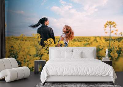 Family photography, mother and daughter look each other love. Happy two together. Long black hair brunette woman fly in wind. Redhead girl enjoy beauty blooming field blue sky. Yellow rapeseed flowers Wall mural