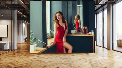 hot young adult, proud and domineering woman dressed in a long scarlet red long dress, sexually demonstrates her naked graceful leg, crouching on the window sill, room in loft stile with mirrors Wall mural