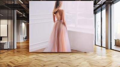 Mysterious young woman princess in elegant beautiful airy luxury long evening trendy dress, bare open back. Sexy Girl graduate long blond hair fly in wind. turned away look out window. Glamour fashion Wall mural