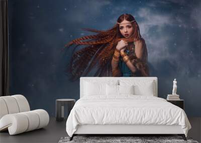 redhead goddess fantasy woman walks in the clouds. Fashion model posing in studio background dramatic winter sky with smoke. Elf princess girl. Long red hair flying in wind snow is falling. Blue dress Wall mural