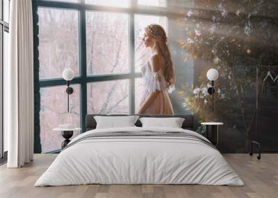 Romantic lady, blonde woman with long hair in white vintage dress stands in dark room, looks out window. Girl bride princess in wedding dress. Elegant hairstyle. Bright rays of sun concept of waiting Wall mural