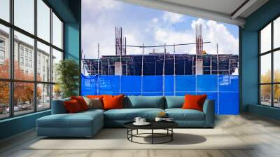 A blue slan surrounds the building under construction. Wall mural