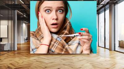 Astonished woman holding thermometer in her hands. Blue background. Virus, sick, flu, covid19, coronavirus concept Wall mural