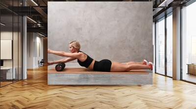 Attractive sportswoman wearing gym clothes, lying on yoga mat with foam roller at hand. Advanced female sport instructor using sport equipment while training. Wall mural