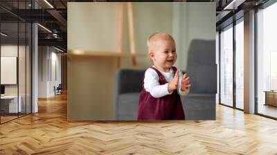 The adorable blonde-haired little girl smiles and claps her hands. The cute little girl is happy. Wall mural