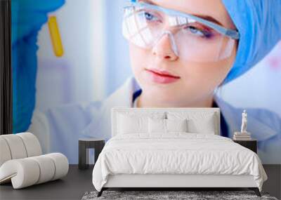 Woman holding test tube. Researcher is surrounded by medical vials and flasks Wall mural