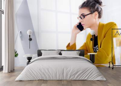 Young business woman talking on the phone while using desktop Wall mural