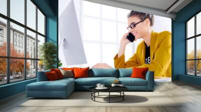 Young business woman talking on the phone while using desktop Wall mural