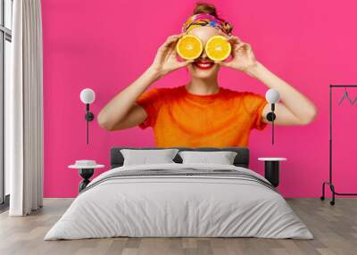 Young woman on a pink background holds a cut orange in her hands and laughs. Colour obsession concept.  Minimalistic style. Stylish Trendy Wall mural