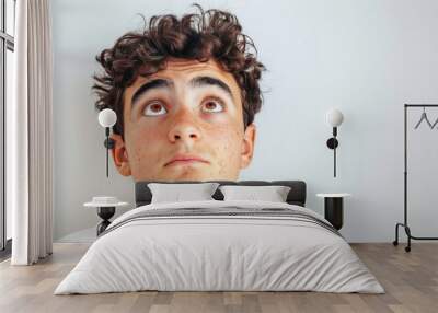 Close up of the face of a young man with curly hair looking up on a white background. Wall mural