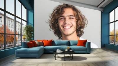 Close up view of a teenage boy with curly hair, isolated on a plain gray background. White shirt. Wall mural