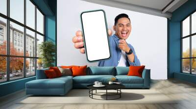 Excited young Asian man in casual shirt showing smartphone with blank screen isolated on white background Wall mural