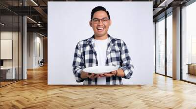 Happy young Asian man in casual shirt holding empty blank plate isolated on white background Wall mural