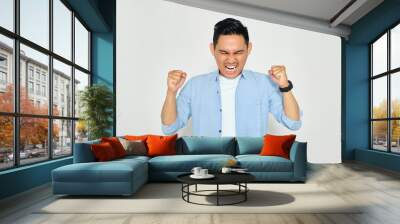 Portrait of angry young Asian man in casual clothes raising hands and screaming with aggressive expression isolated on white background Wall mural