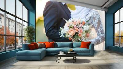 The bride and groom hold a wedding bouquet of luxurious and beautiful flowers, Hold the hands of the newlywed couple close up. Wall mural