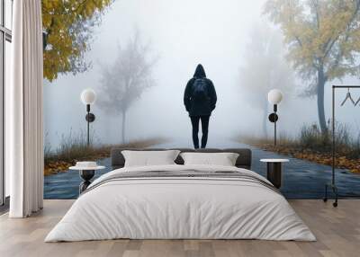 A lone person in a hooded jacket walks down a foggy path lined with autumn trees, creating a mysterious atmosphere. Wall mural