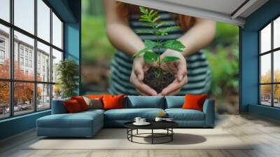 A young woman presents a small green plant seedling cupped in her hands, signifying growth and environmental conservation. Wall mural