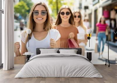 Three smiling young women holding shopping bags, enjoying a day out in a vibrant shopping district. Wall mural