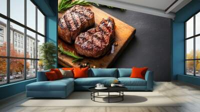 Two perfectly grilled steaks with grill marks on a wooden board, garnished with fresh rosemary and peppercorns. Wall mural