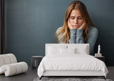 Young woman sits against a wall, head in hands, showing feelings of sadness and frustration in an indoor setting. Wall mural