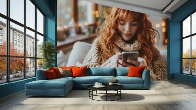 Young woman with red hair enjoying cozy indoor time, using a smartphone, in a warmly lit, festive home setting. Wall mural