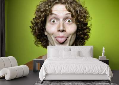 Young funny man shows his tongue, studio shot over green backgro Wall mural