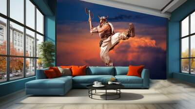 crazy strong viking with traditional costume attacking and jumping from sky in the sunset background. looking at camera with angry eyes.  Wall mural