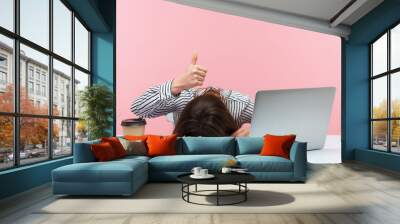 I am fine. Extremely tired sleepy woman lying on table with laptop and cup of coffee showing thumbs up, exhausted with overwork, vitamin deficiency. Indoor studio shot isolated on pink background Wall mural