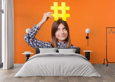 Popularity in social media. Portrait of funny brunette woman wearing checkered casual shirt holding large big yellow hashtag sign on head as crown. indoor studio shot isolated on orange background Wall mural