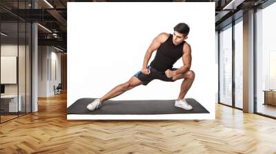 Portrait of a young adult athletic man in sports clothing doing leg stretching exercises on yoga mat before workout, healthy lifestyle. Indoor studio shot isolated on white background. Wall mural