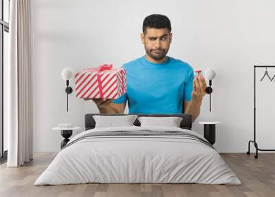 Portrait of pensive confused unshaven man wearing blue T- shirt standing holding two present boxes, little and big, thinking what to choose. Indoor studio shot isolated on gray background. Wall mural