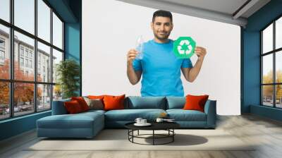 Portrait of smiling happy handsome unshaven man wearing blue T- shirt standing holding green recycling sign, planet protection. Indoor studio shot isolated on gray background. Wall mural